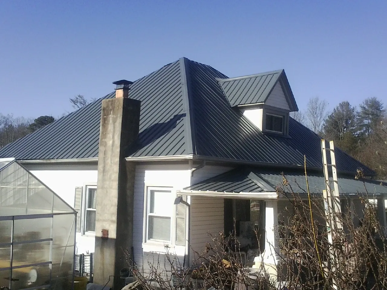 Dark blue standing seam metal roof on a white farmhouse with dormer — Slate & Tile Roof Repair by Roofing Brothers in North Jackson