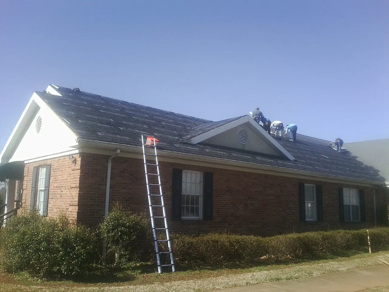 Crew tearing shingles off a brick ranch roof with a ladder set — Emergency Roof Repair work by our crew in North Jackson