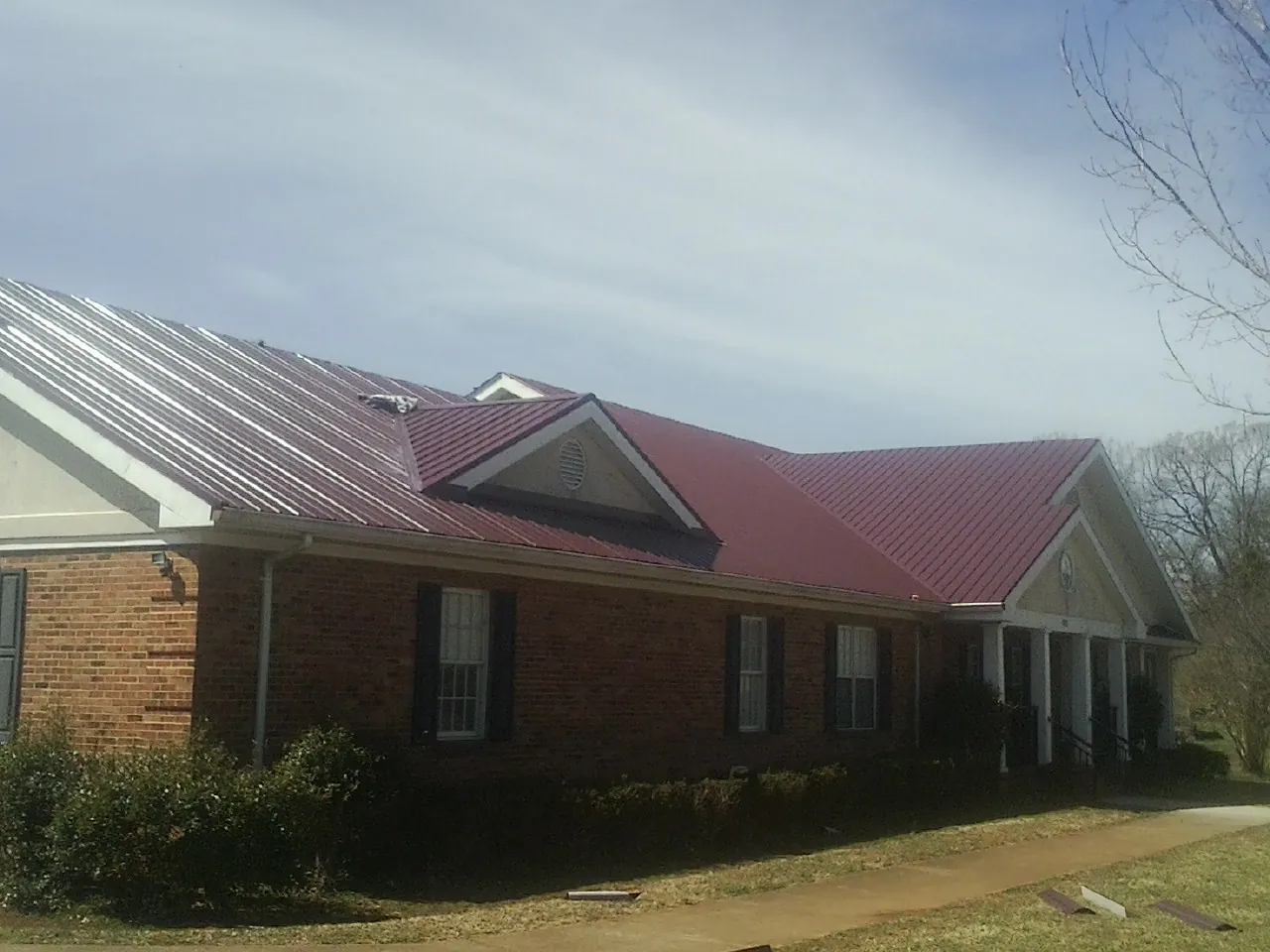 Red metal roof with gabled entries on a long brick building, from a Hail Damage Roof Repair job in North Jackson