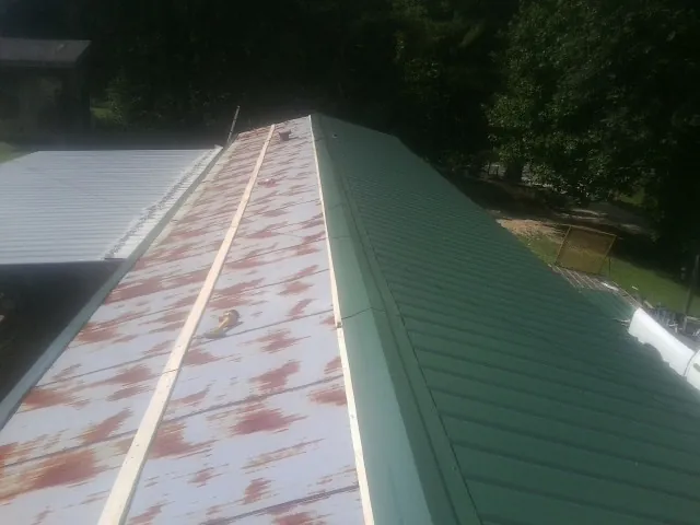 Old rusted panels beside newly installed green metal roofing — Wind Damage Roof Repair by Roofing Brothers in North Jackson