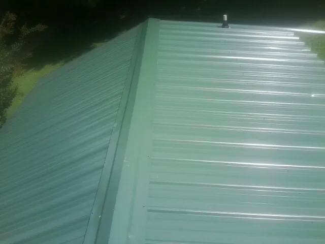 New green metal panels meeting at the ridge of a roof — Flat Roof Repair work by our crew in North Jackson