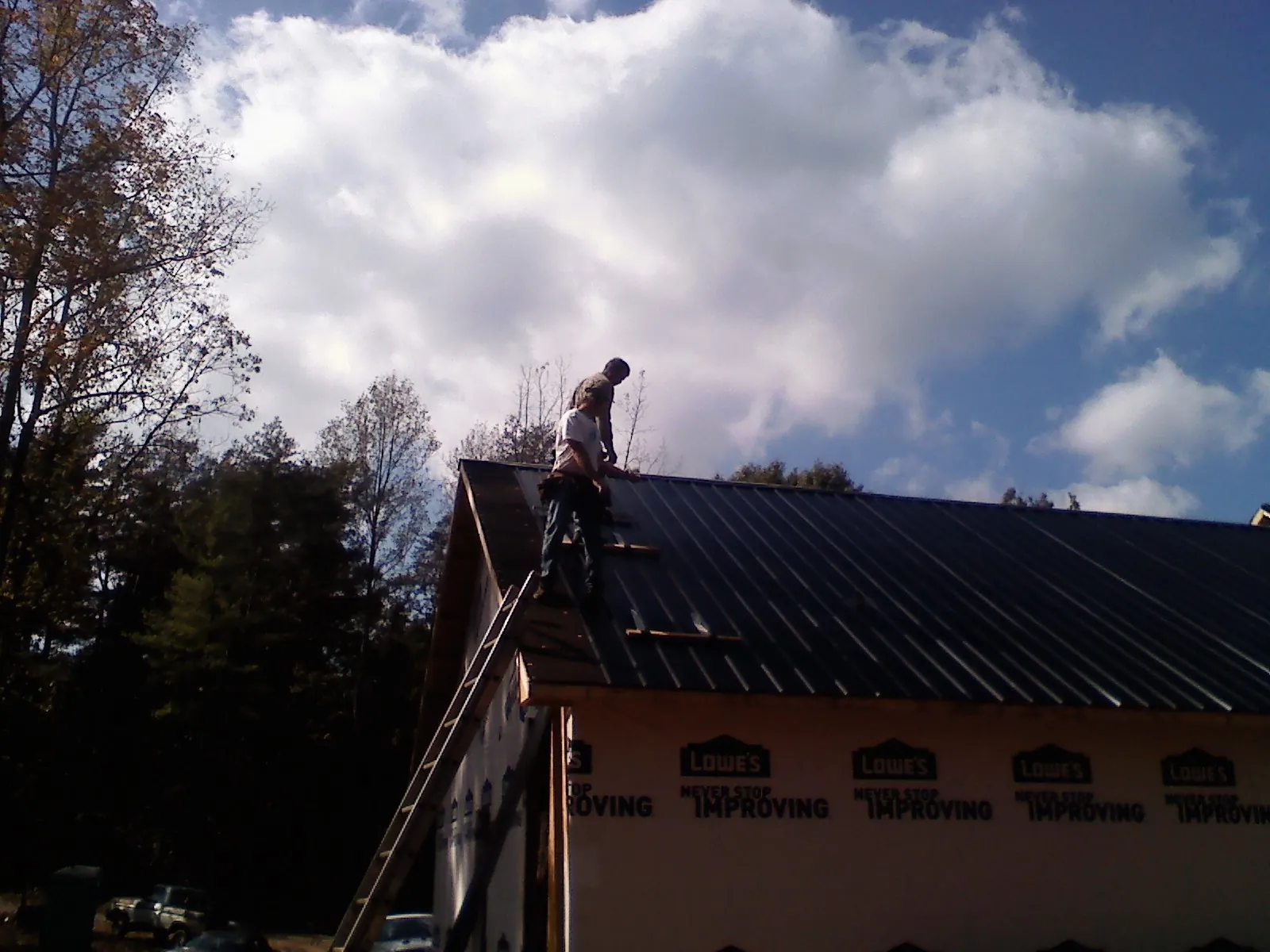 Roofer fastening dark metal panels high against a cloudy sky, from a Roof Inspection job in North Jackson