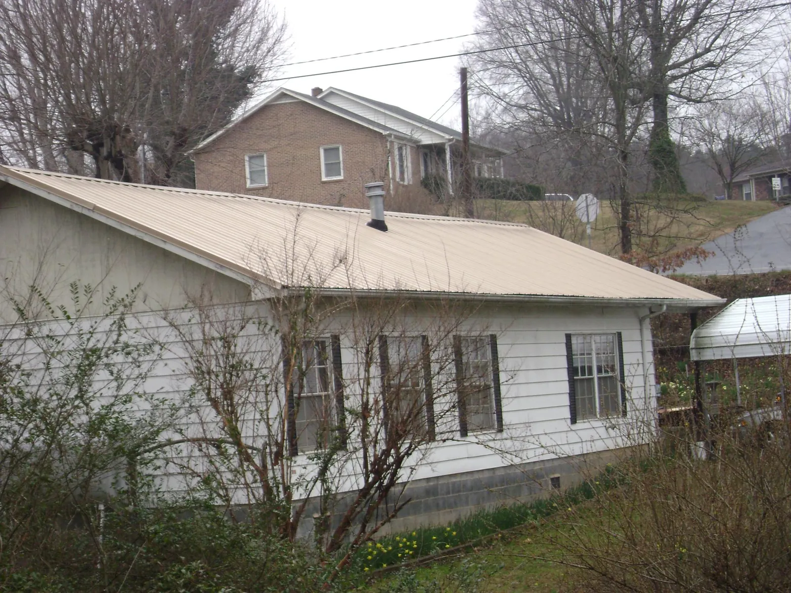 Tan metal roof on a white sided house set into a hillside — Commercial Roofing by Roofing Brothers in North Jackson