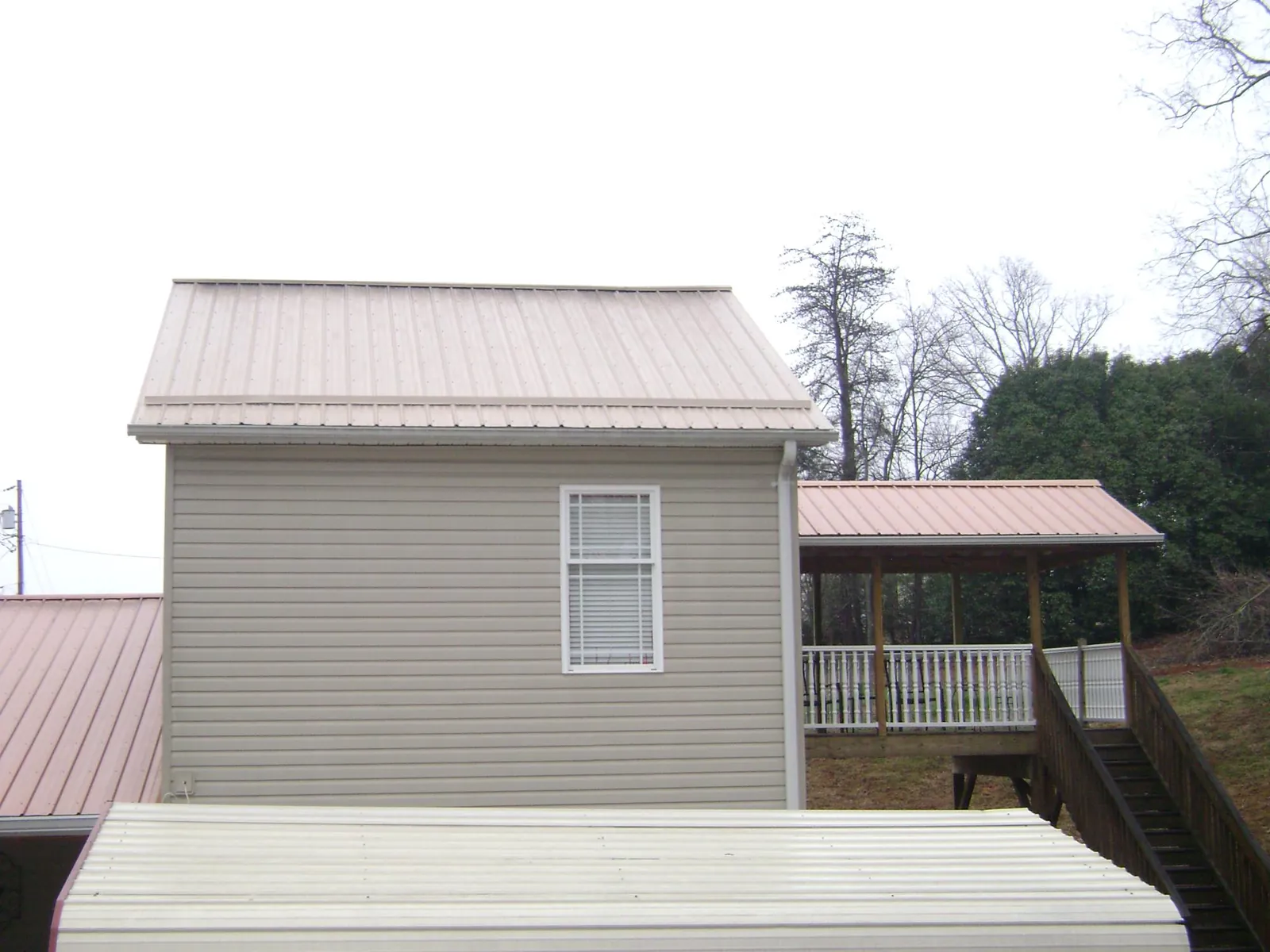 Tan metal roofs on a two story addition and attached porch, from a Roof Replacement job in North Jackson